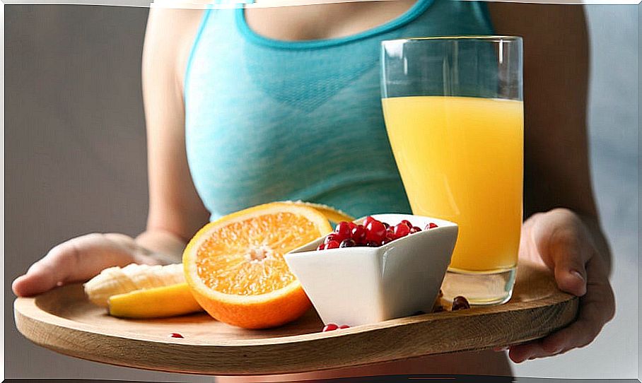 Woman carrying a tray of food with juice, oranges and a bowl of red berries after exercising.